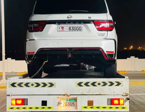 Rear view of a white Nissan Patrol SUV secured on a Perfection Car Recovery flatbed truck at night in Abu Dhabi.