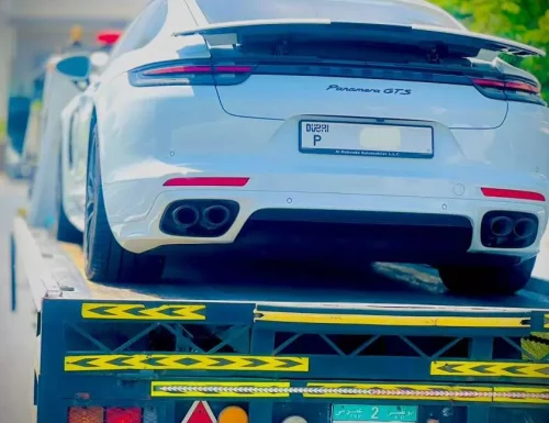 A white Porsche Panamera GTS luxury sedan being transported on a Perfection Car Recovery flatbed tow truck in Abu Dhabi.
