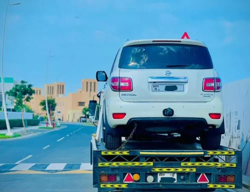 A white Nissan Patrol SUV being recovered by a flatbed tow truck on a street in Abu Dhabi.