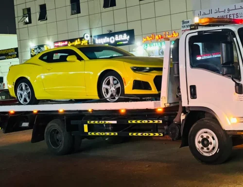 A yellow Chevrolet Camaro sports car being safely transported on a Perfection Car Recovery flatbed truck at night in Abu Dhabi.